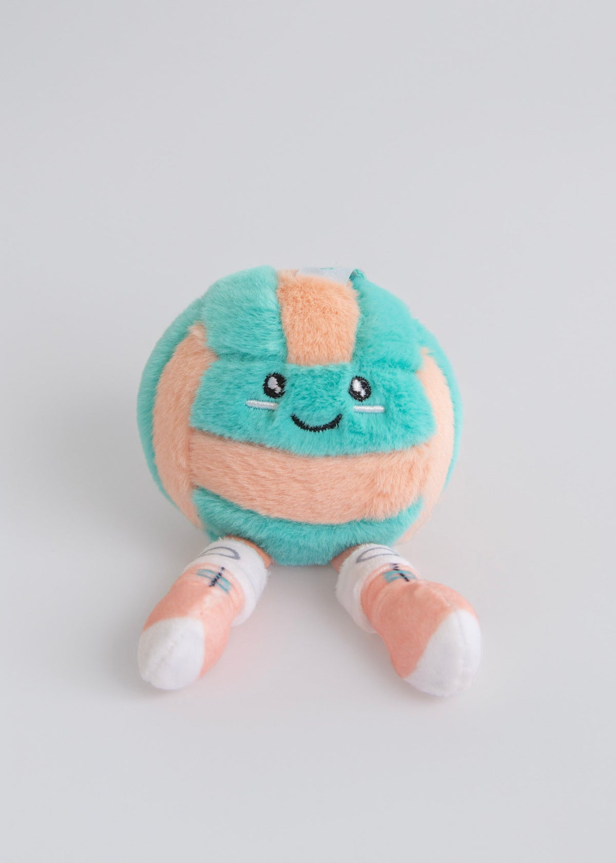 Plush toy resembling a volleyball with a smiling face on a light gray background