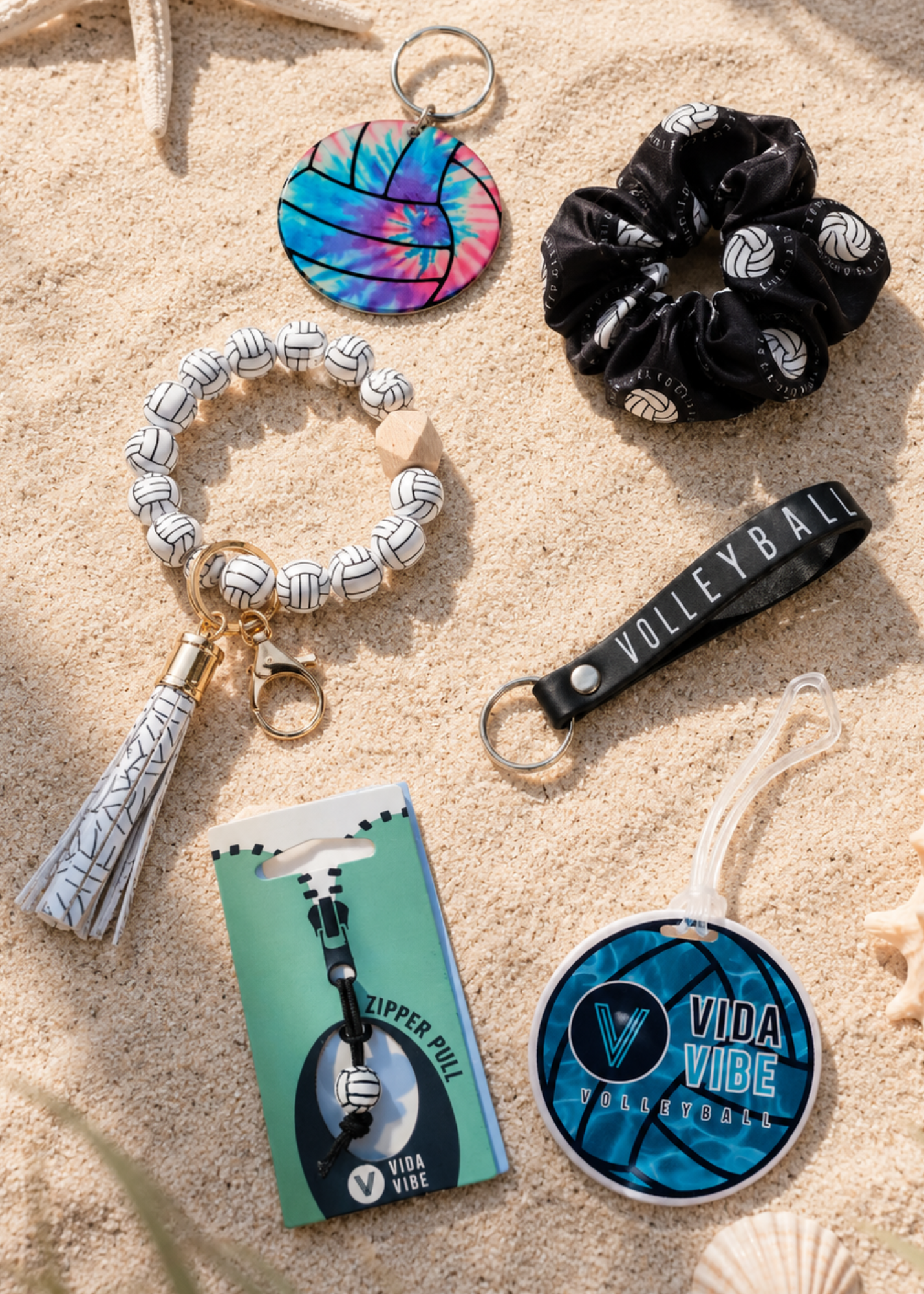 Collection of volleyball-themed accessories including a keychain, scrunchie, and lanyard on sand.