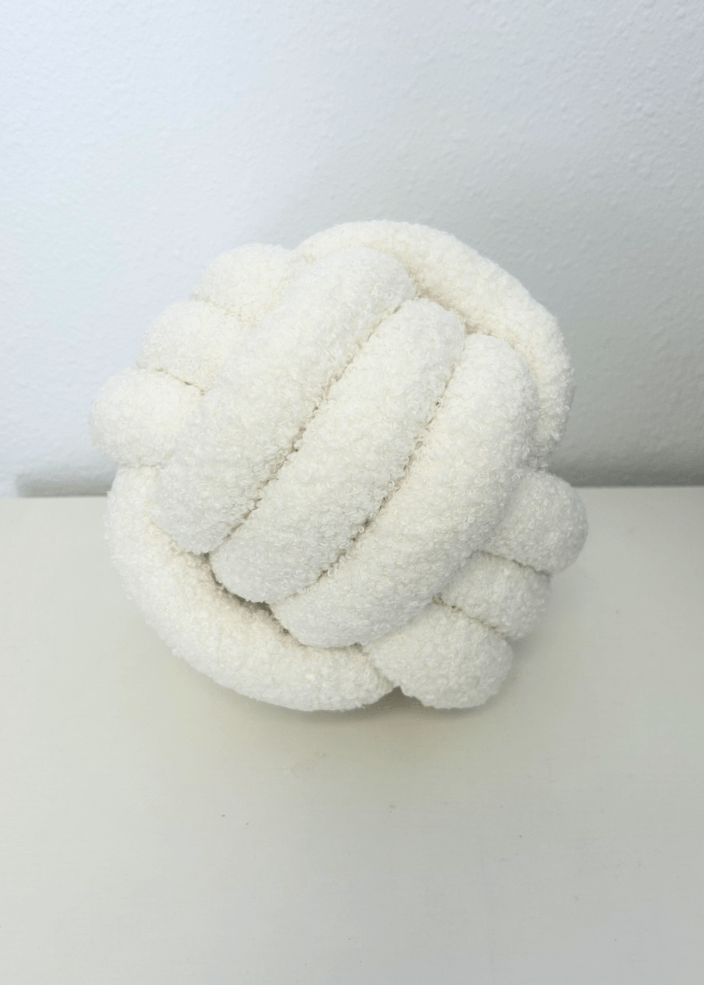 White knitted knot volleyball pillow on a white surface with a white background