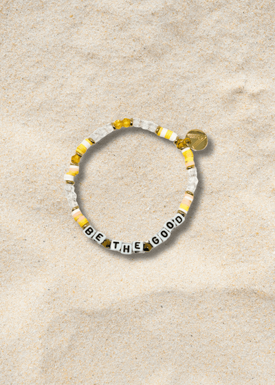 Bracelet with 'BE THE GOOD' message on a beige sand background