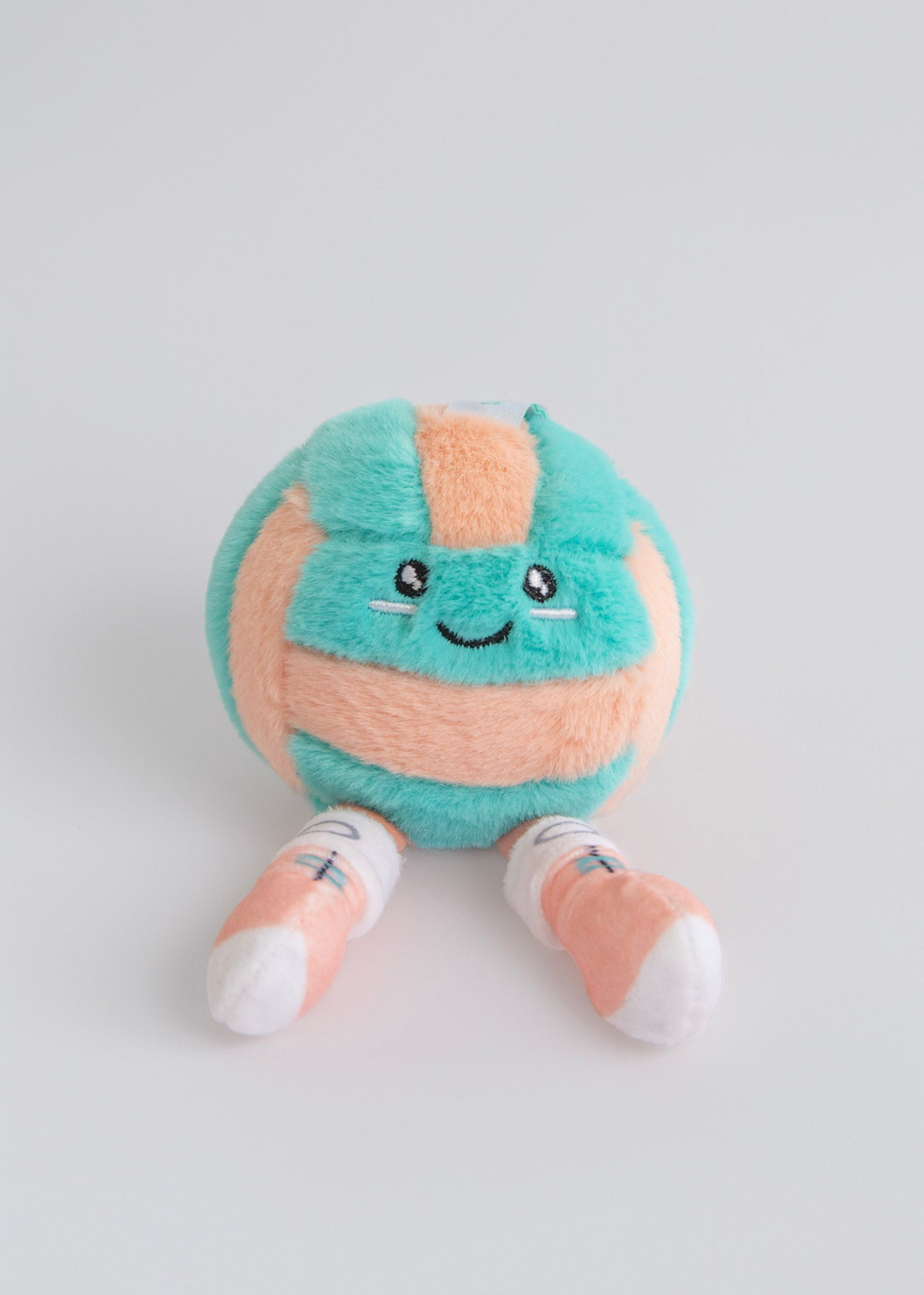 Plush toy resembling a volleyball with a smiling face on a light gray background