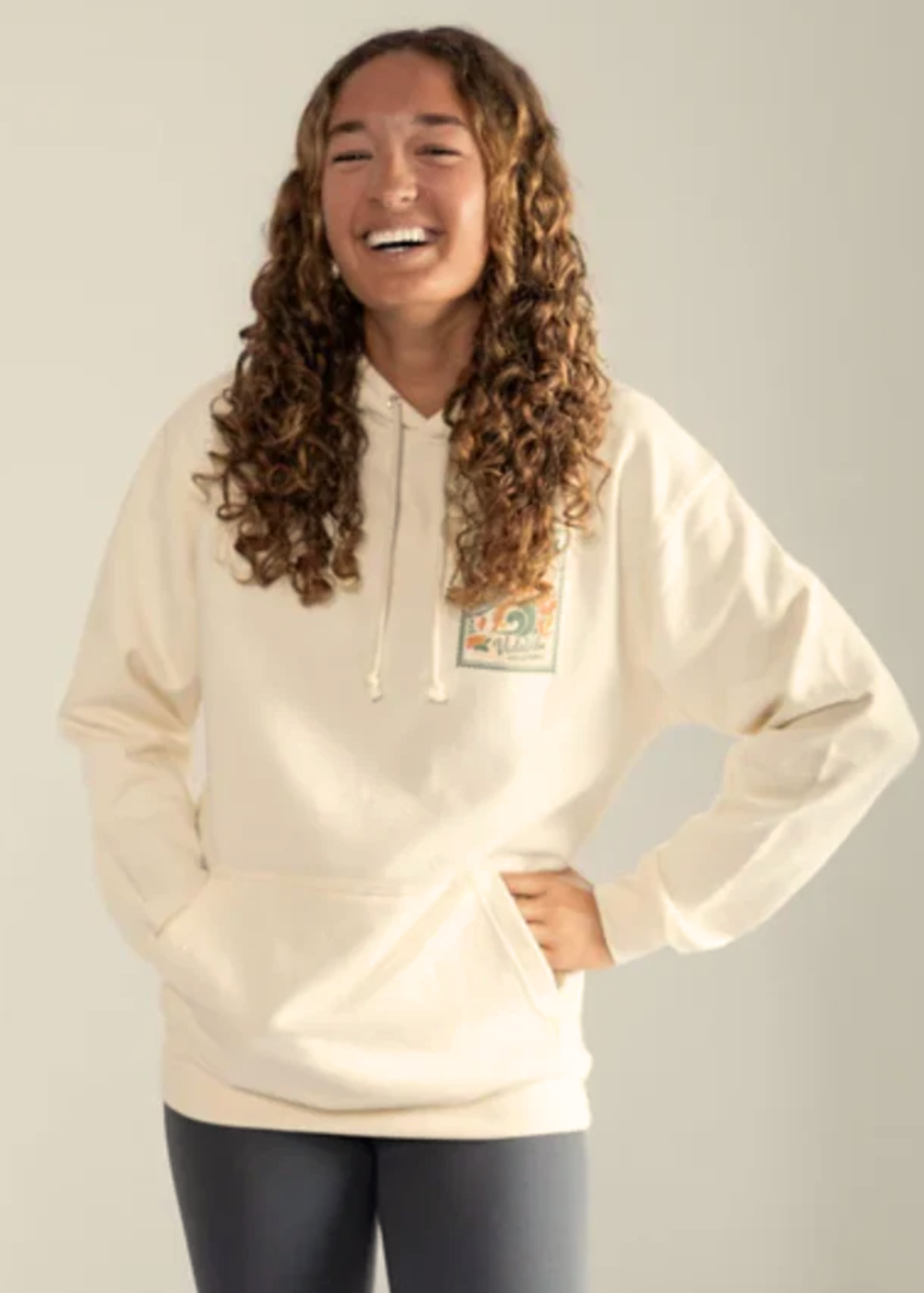 Girl wearing a cream volleyball hoodie with a logo on a plain background