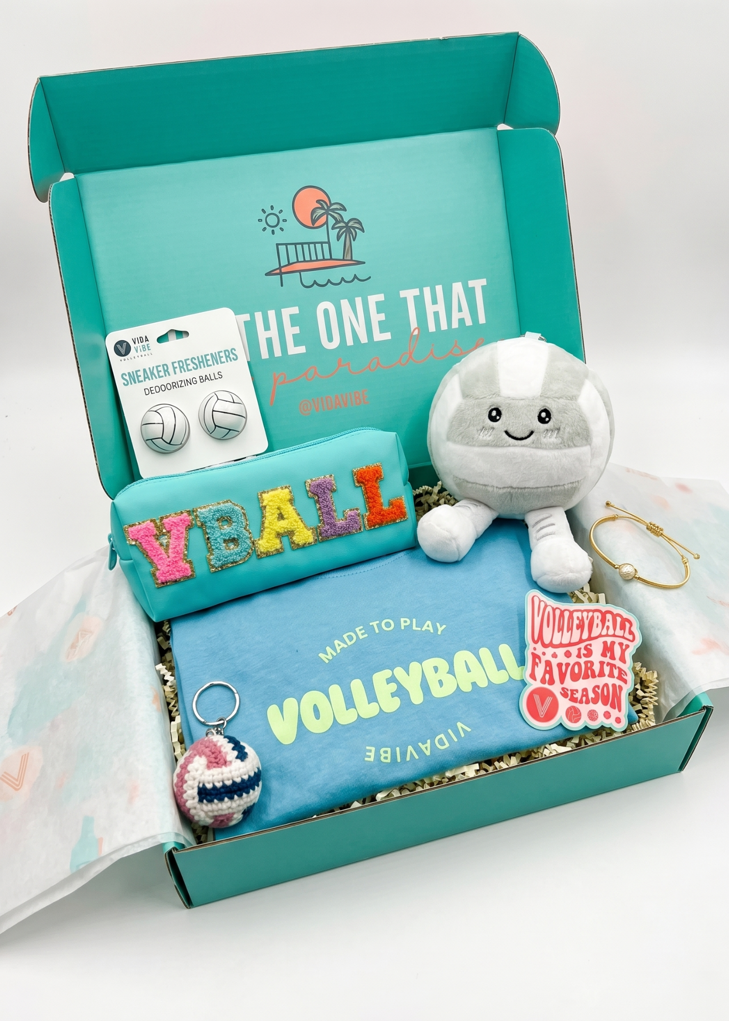 Open teal box containing a plush toy, greeting card, and other items with 'Volleyball' theme.