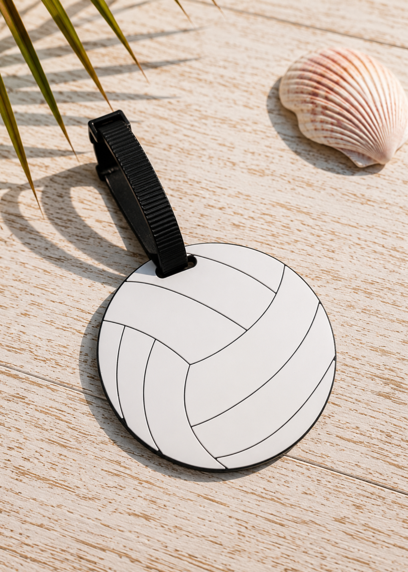 A round luggage tag featuring a white volleyball pattern with black outlines, attached to a black strap, displayed on a light wood surface with a seashell and palm leaves in the background.