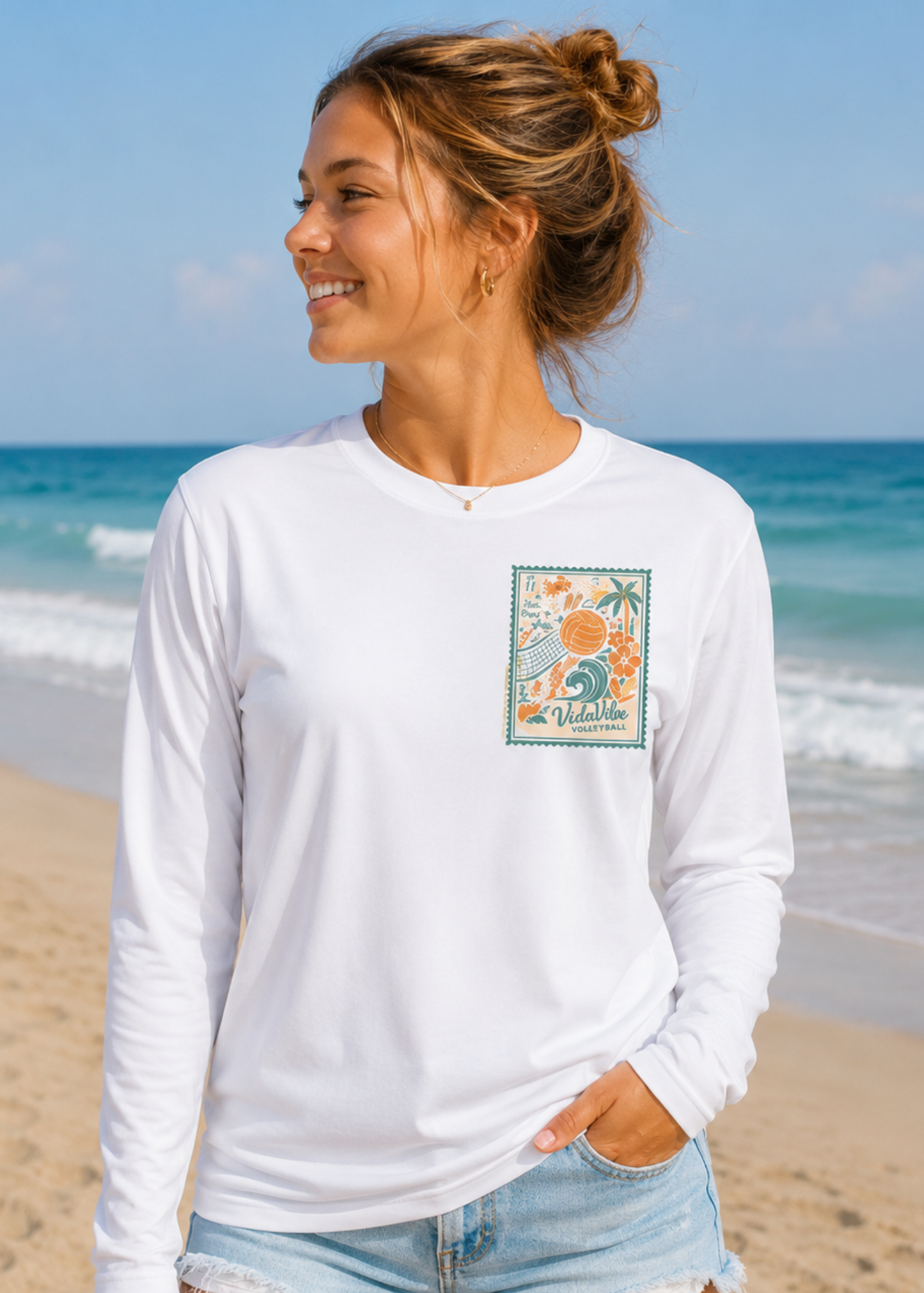 A woman wearing a white long-sleeve t-shirt with a colorful tropical volleyball graphic on the left chest.