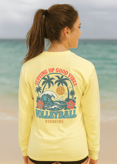 Woman wearing a yellow long-sleeve shirt with volleyball design and text on a beach.