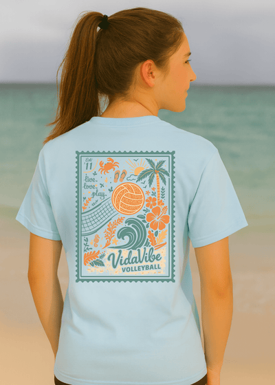 Woman wearing a light blue t-shirt with a beach-themed design on a beach.