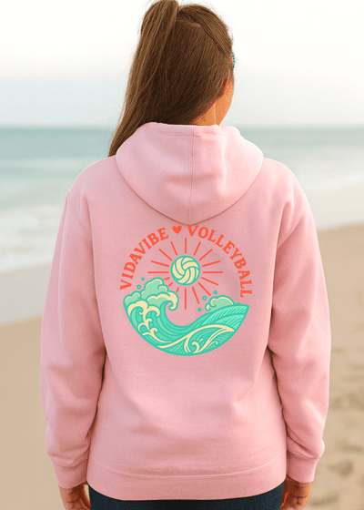 Person wearing a pink hoodie with 'Vibedrive Volleyball' design on a beach